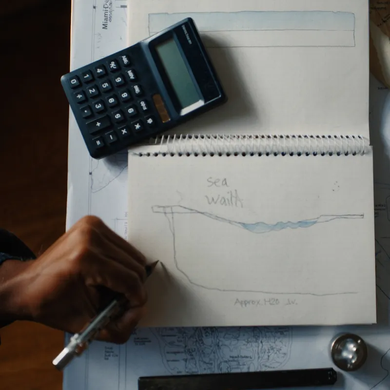 Hands sketching a seawall cross-section on graph paper with calculator and Miami-Dade map